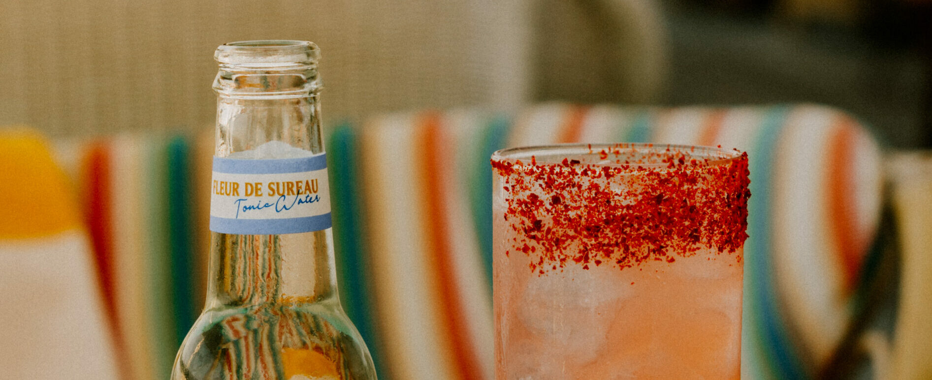 Un verre de cocktail garnit de poudre de piment sur le bord et une bouteille de Tonic Water Fleur de Sureau